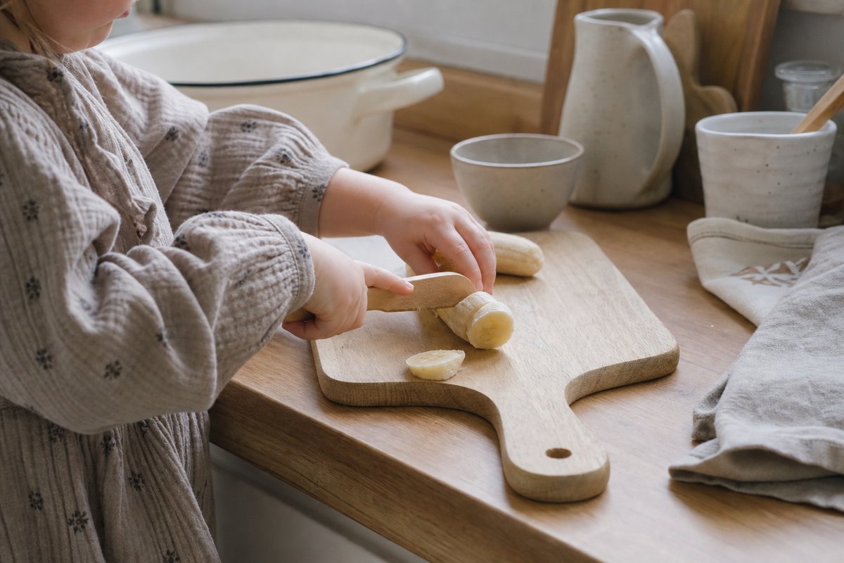 Kinderhände schneiden eine Banane mit einem Holzmesser auf einem Brett