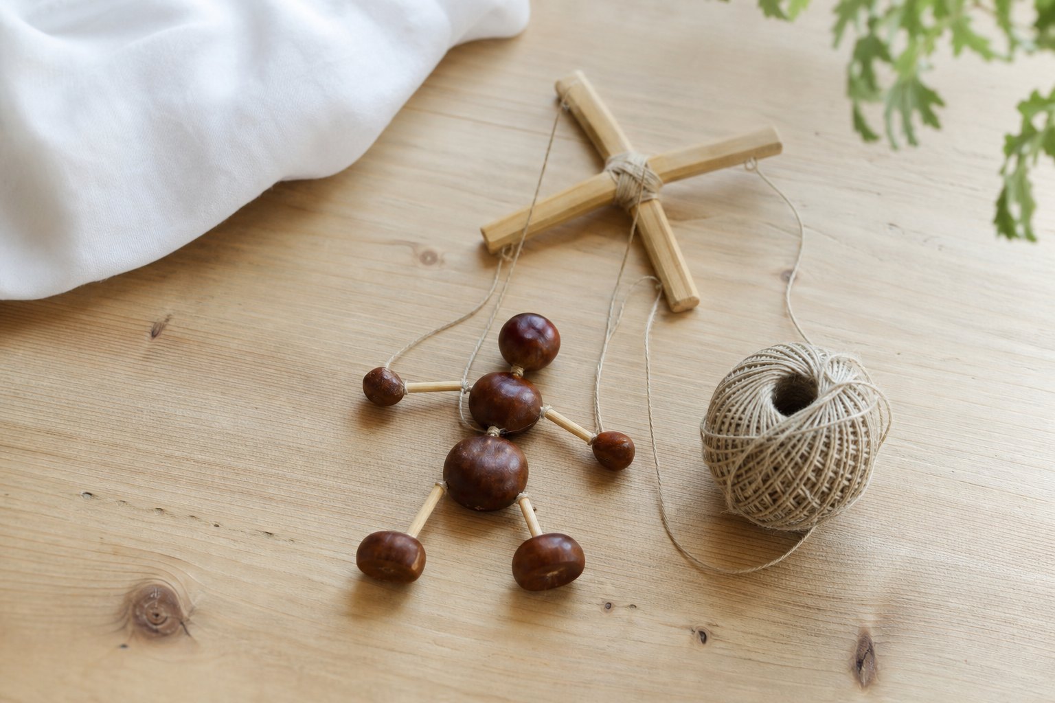 Auf einem Holztisch: eine kleine Marionette aus Kastanien, die mit Fäden verbunden sind, daneben ein kleines Holzkreuz und ei