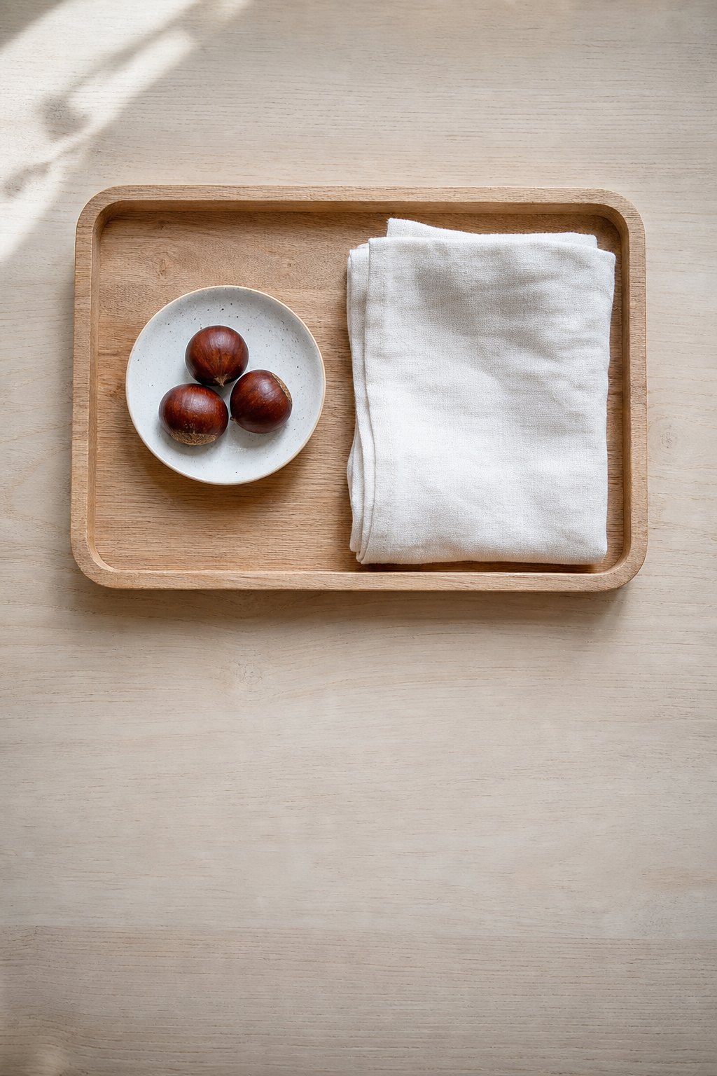 Montessori Tablett mit eine kleine Schale mit drei glänzenden Kastanien und ein zusammengelegtes weiches Tuch