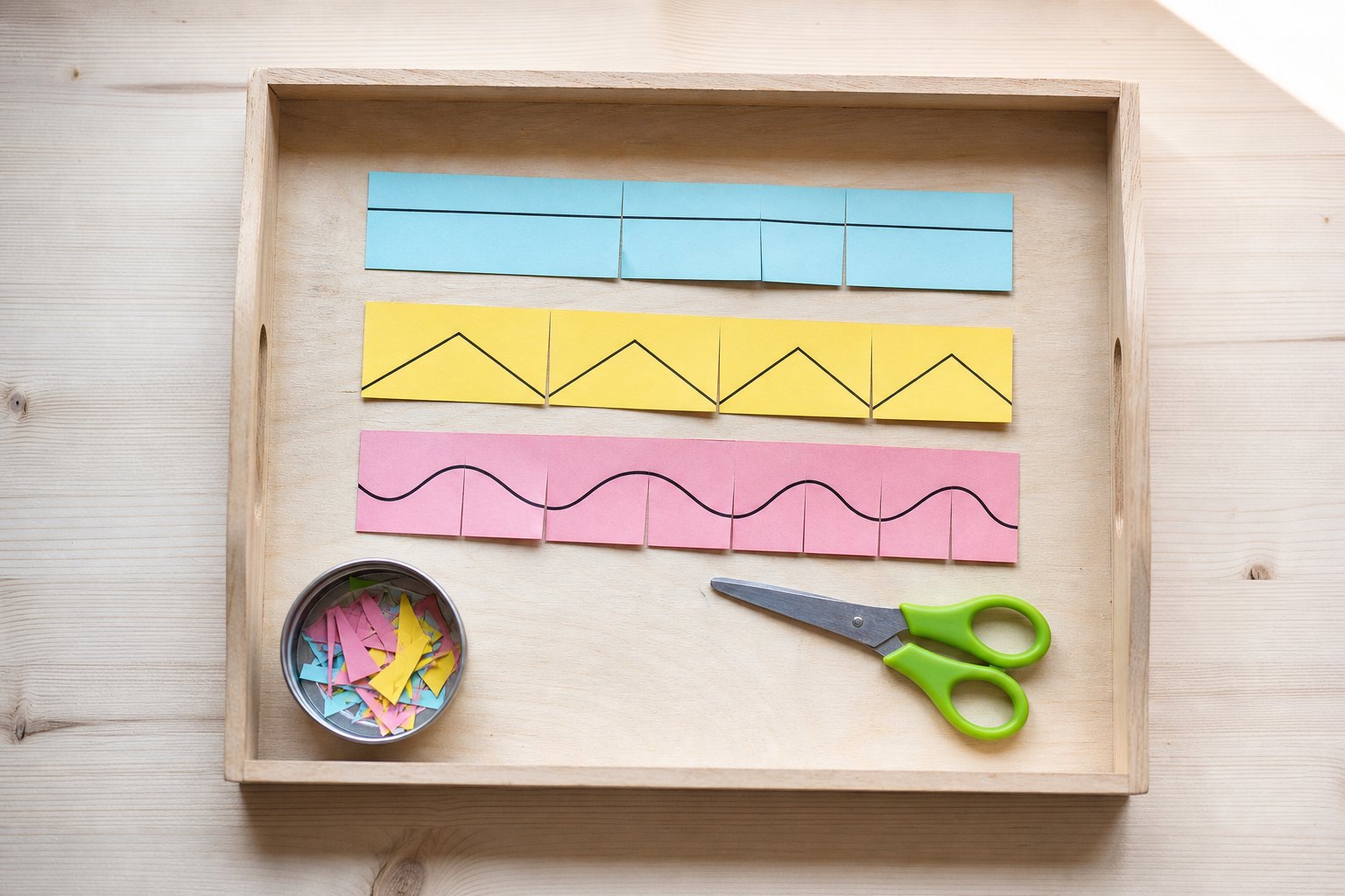 Montessori Tablett mit drei bunte Papierstreifen mit aufgemalten schwarzen Linien, einer gerade, einer im Zickzack, einer gew