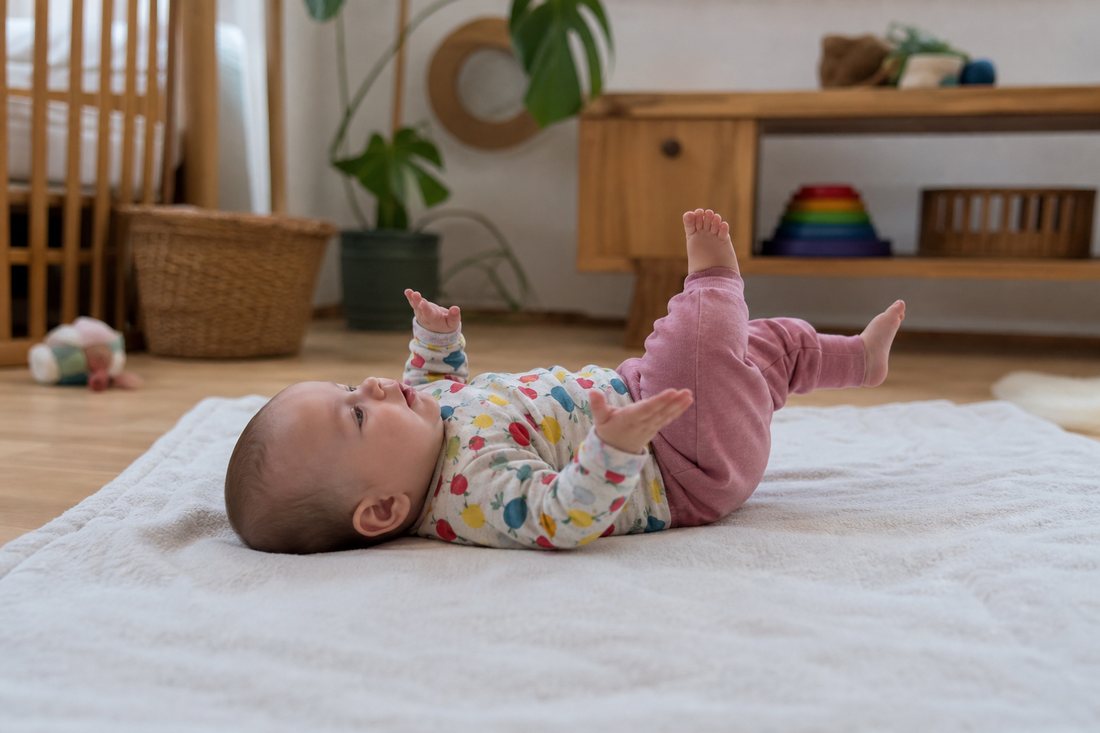 Ein Saeugling liegt frei auf einer Decke am Boden und bewegt Arme und Beine, niemand stuetzt oder haelt ihn.