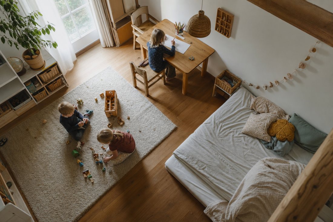 Ein Kinderzimmer von oben gesehen mit klar getrennten Bereichen: Teppich zum Spielen, Tisch zum Arbeiten, Matratze zum S