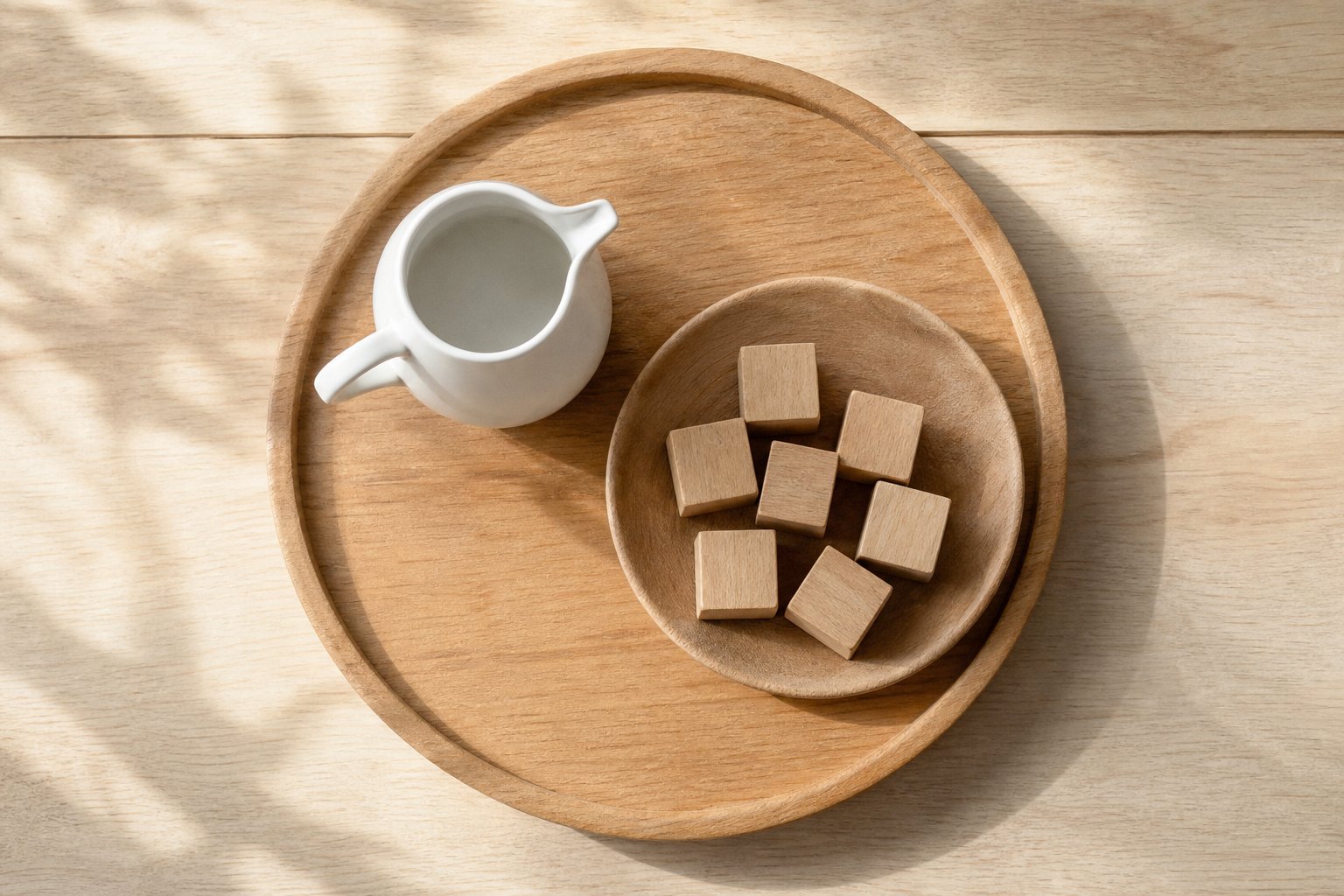 Draufsicht auf ein rundes Holztablett, darauf ein kleiner weisser Keramikkrug und eine flache Holzschale mit sieben unlackier