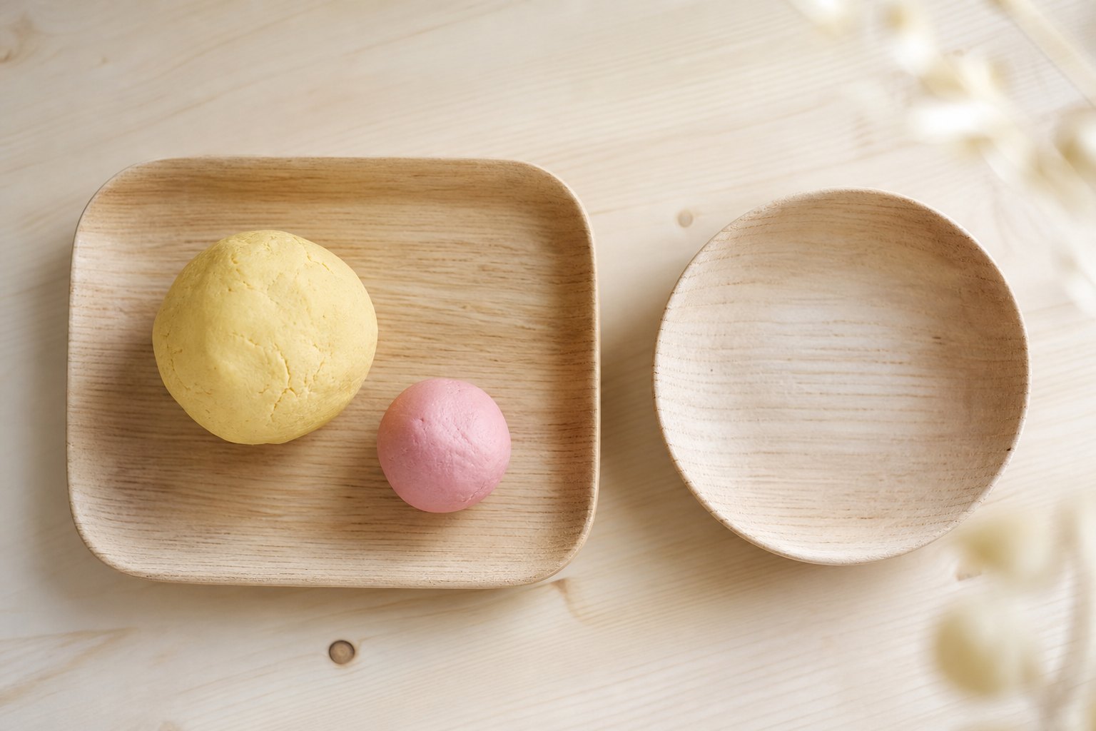 Draufsicht auf ein Holztablett, darauf eine Kugel gelblicher selbstgemachter Knete und eine kleinere Kugel in Rosa, daneben e