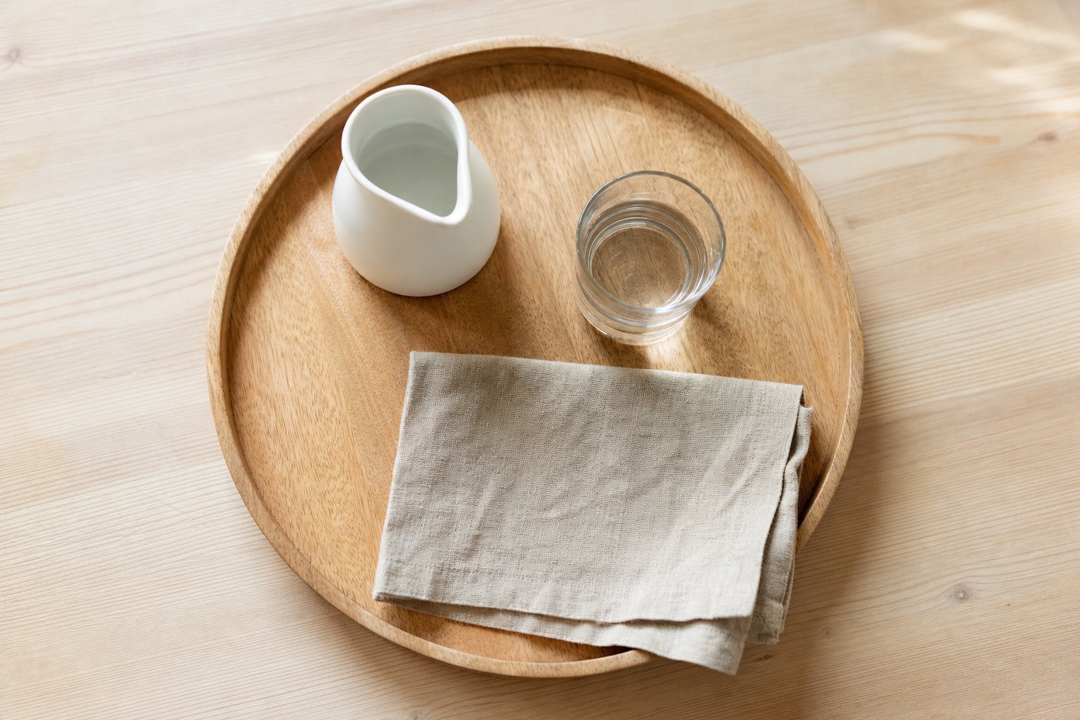 Draufsicht auf ein Holztablett mit erhoehtem Rand, darauf ein kleiner weisser Keramikkrug mit Wasser, ein kurzes dickwandiges