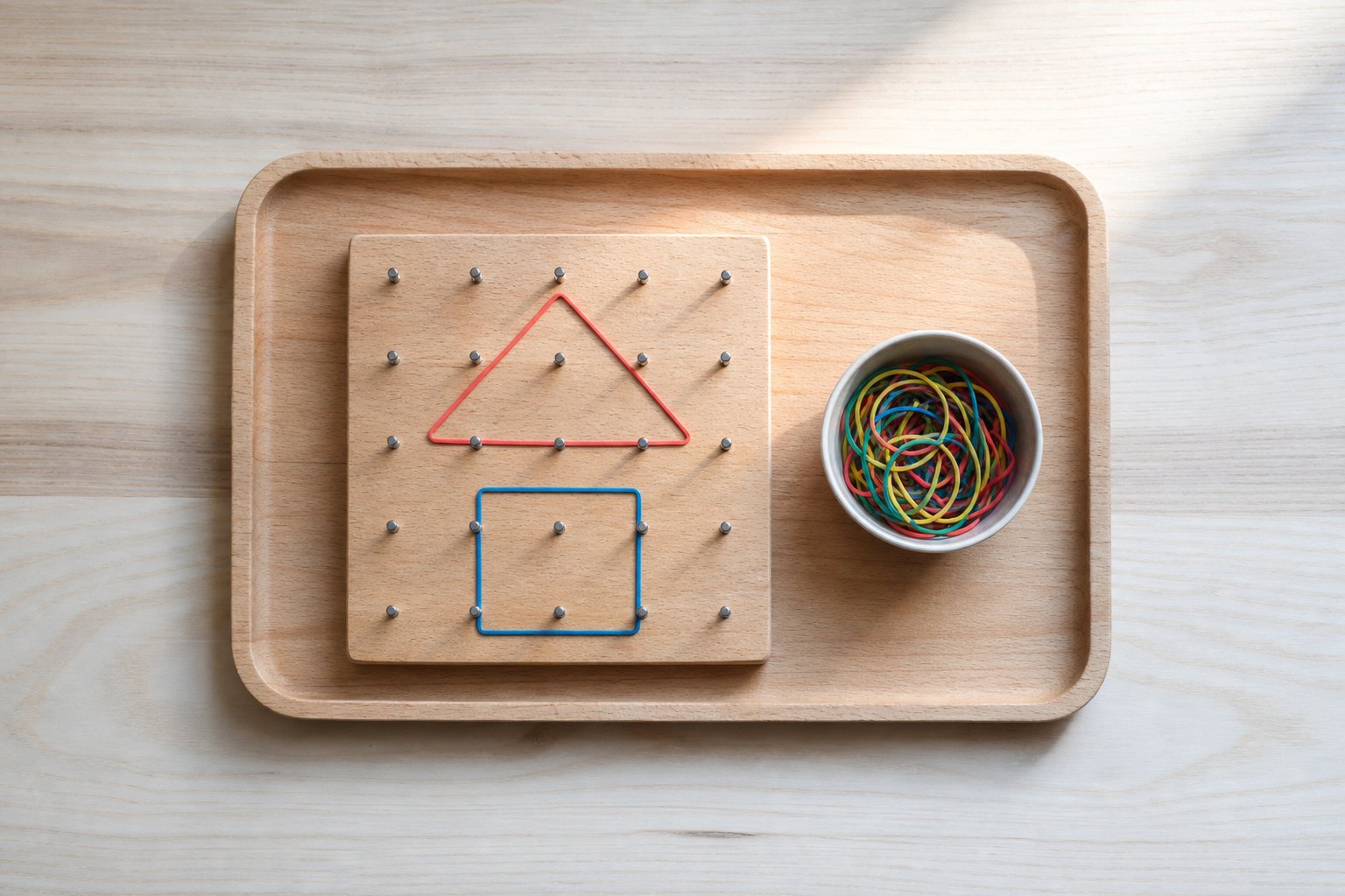 Montessori Tablett mit ein quadratisches Holzbrett mit sechzehn Naegeln in gleichmaessigem Raster, darauf ein rotes Gummiband