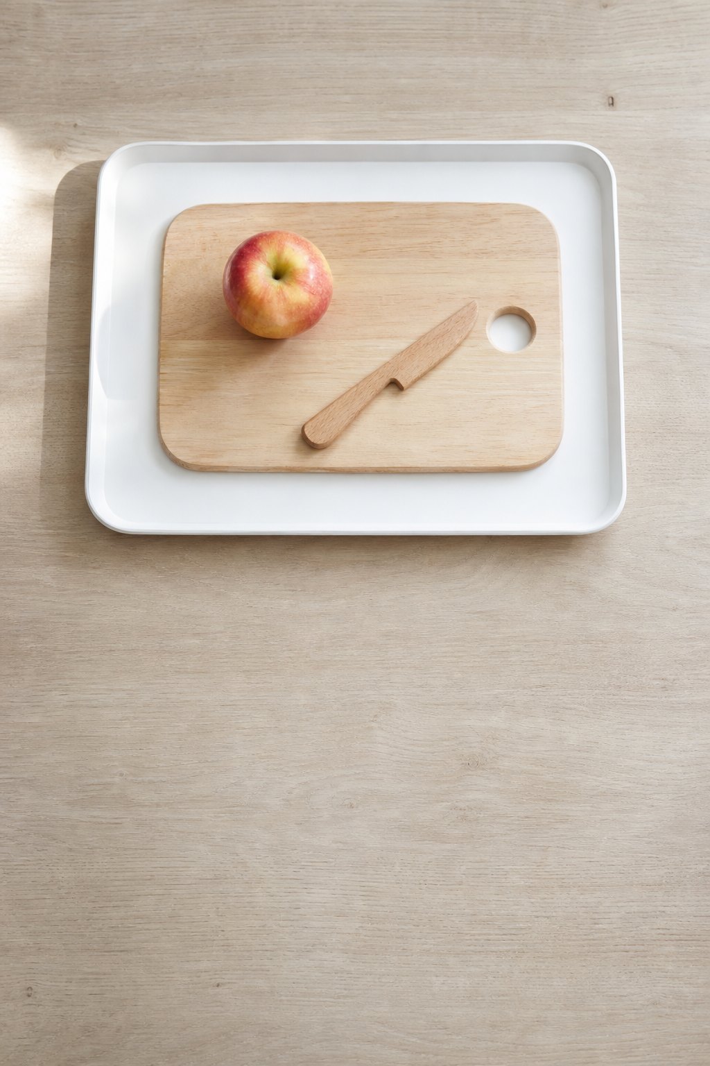Apfel, Schneidebrett und Kindermesser aus Holz auf einem Tablett