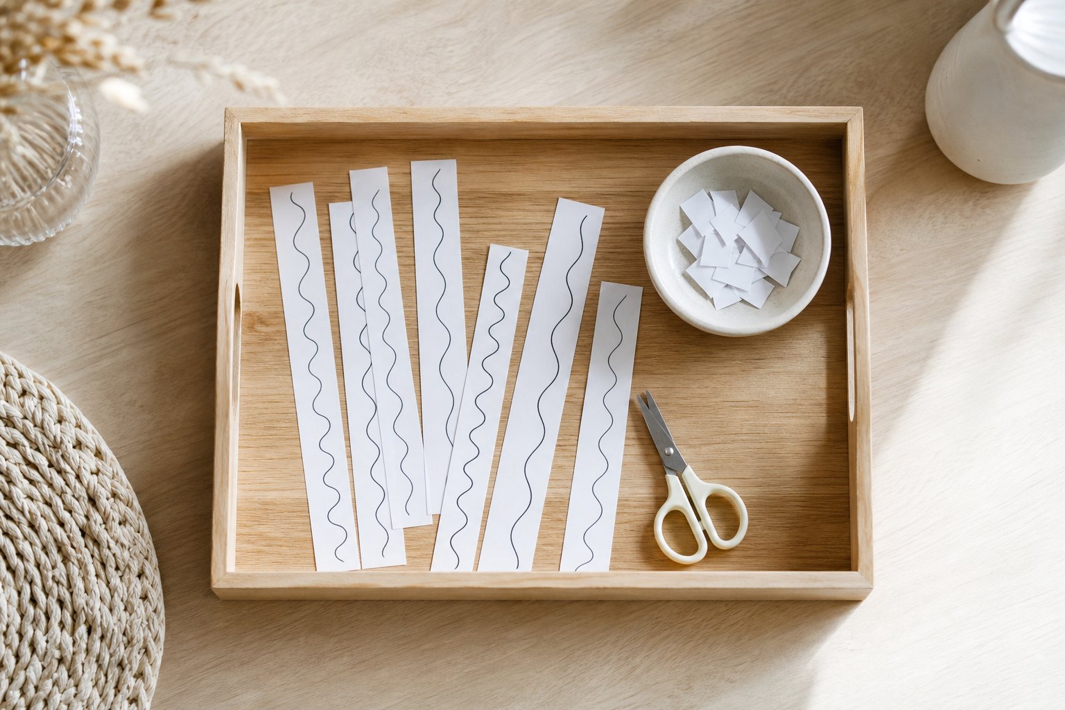 Montessori Tablett mit schmale weiße Papierstreifen mit aufgedruckten Wellenlinien, eine kleine Kinderschere und eine Schale 