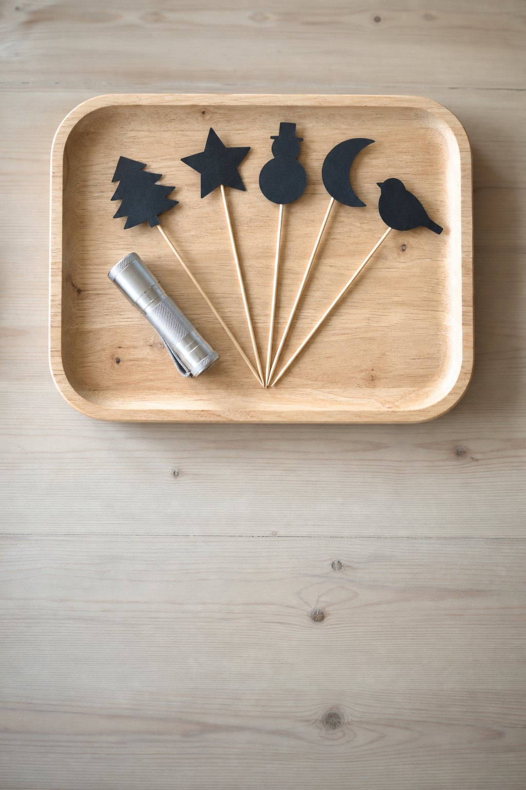Tablett mit einer kleinen Taschenlampe und schwarzen Schattenformen an Holzspießen