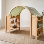Waldorf Spielständer aus hellem Holz mit grünem Tuch als Dach in einem Kinderzimmer