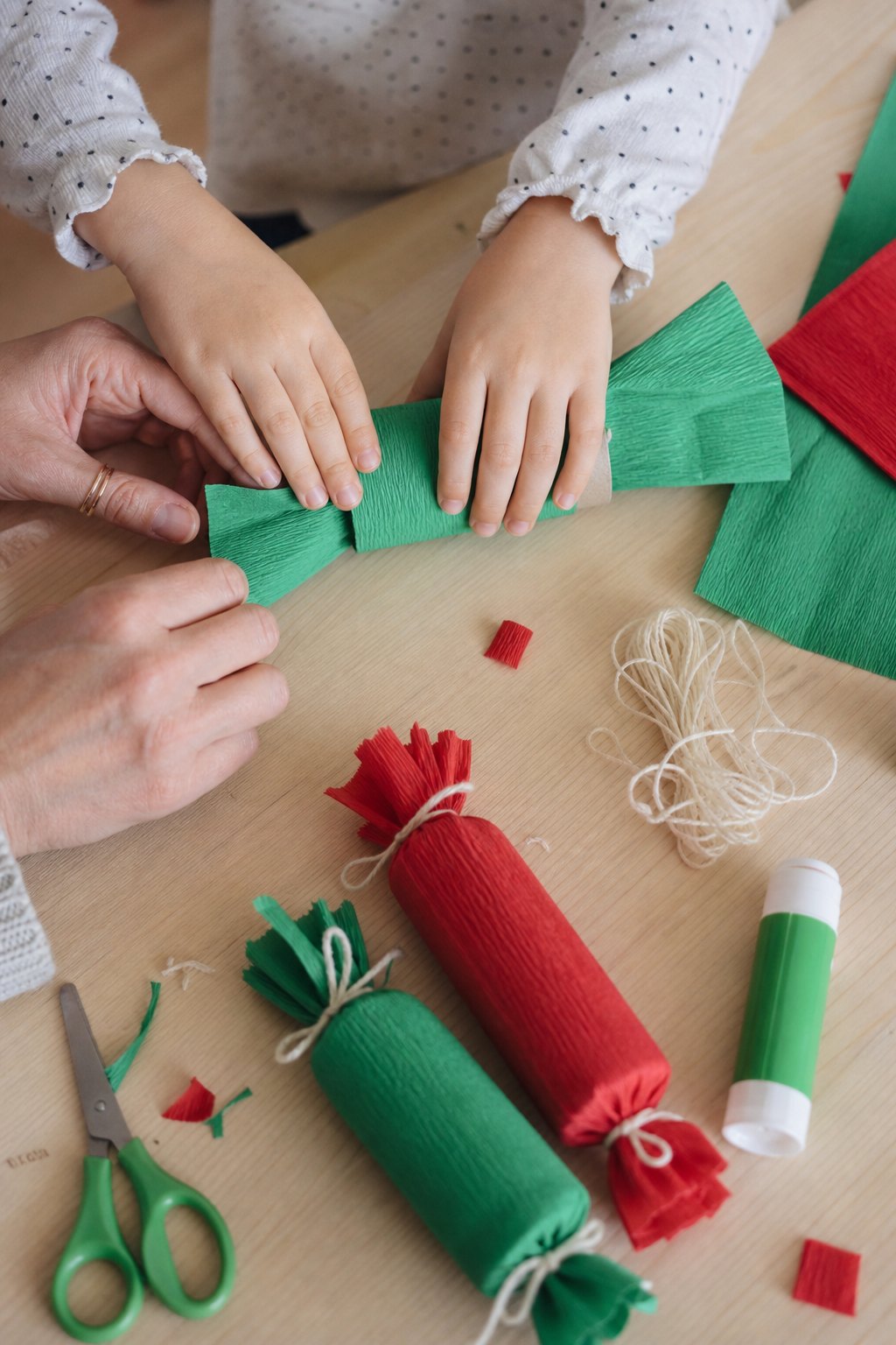 Kinderhände rollen eine Klopapierrolle in grünes Krepppapier ein