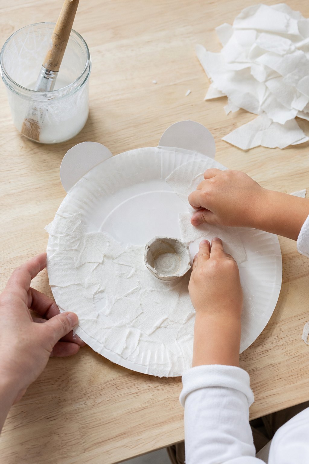 Kinderhände kleistern Fetzen aus Küchenpapier auf den Pappteller mit Schnauze