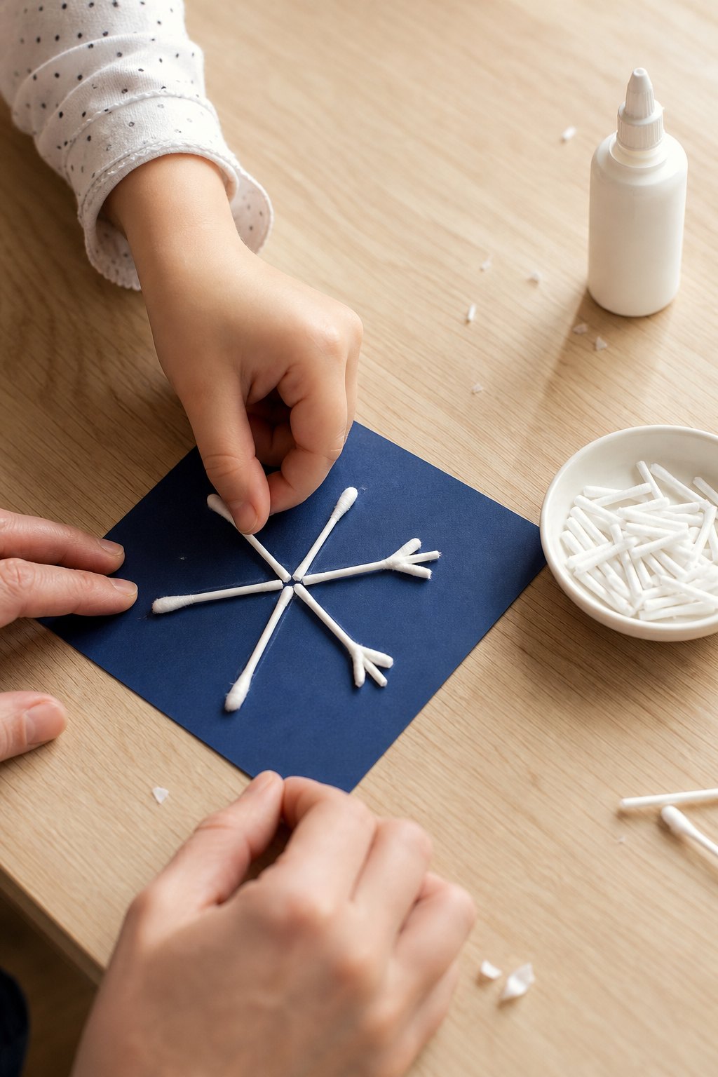Eine Kinderhand legt ein halbes Wattestäbchen an die Schneeflocke auf blauem Karton