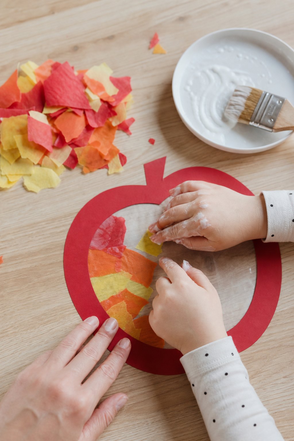 Kinderhände kleben gerissene Transparentpapier-Schnipsel in den Apfelrahmen