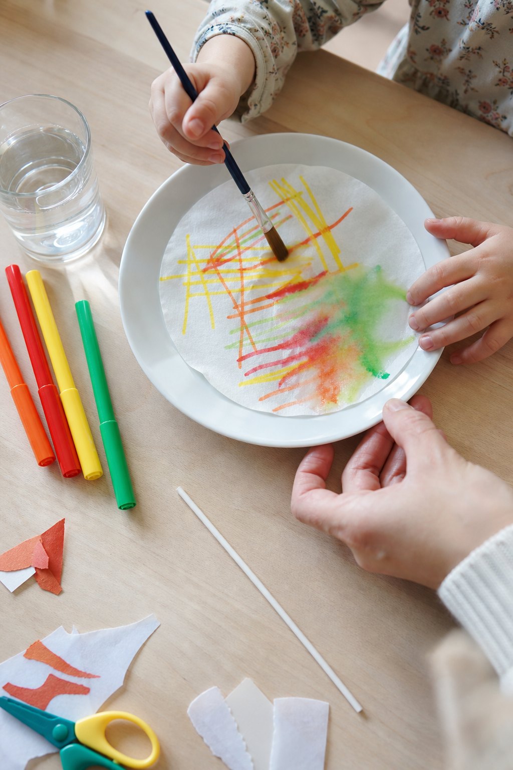 Eine Kinderhand tupft Wasser auf den bemalten Kaffeefilter, die Farben verlaufen