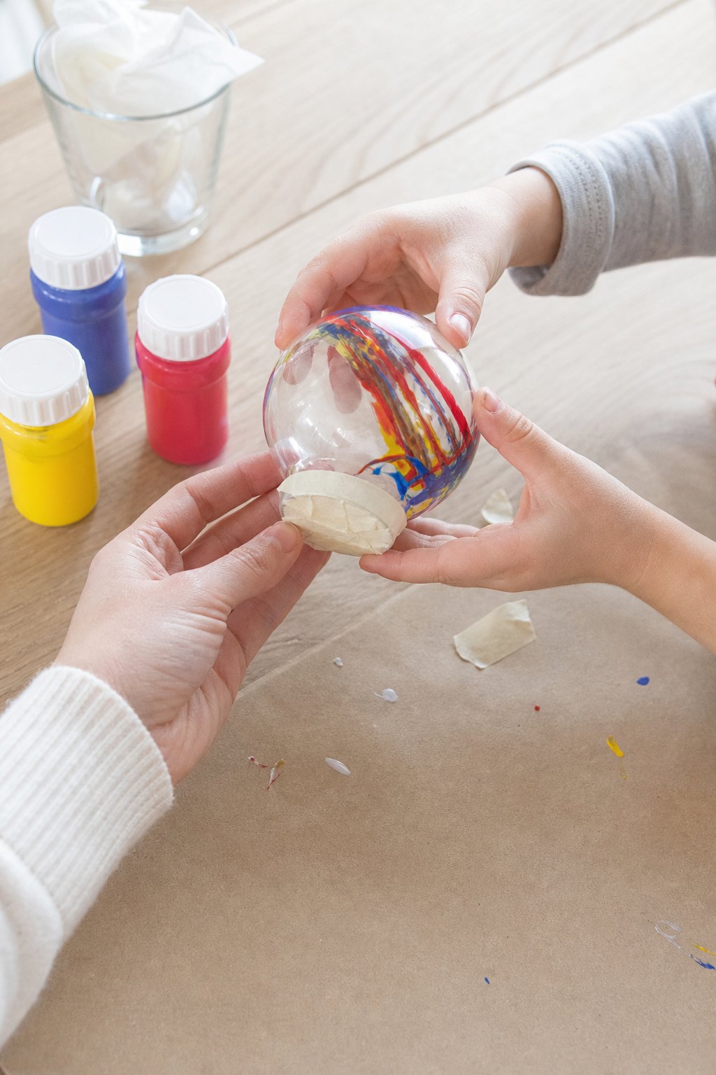 Zwei Kinderhände schwenken eine Kunststoffkugel mit bunter Farbe darin