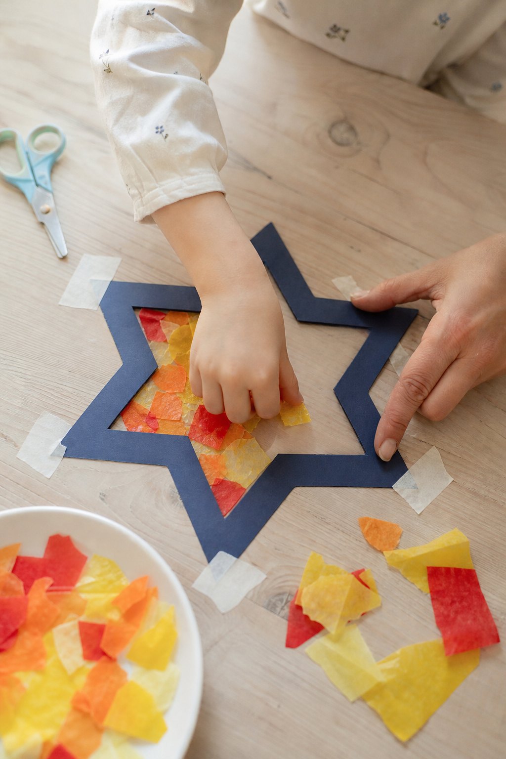 Eine Kinderhand drückt Transparentpapier-Schnipsel in den Sternrahmen