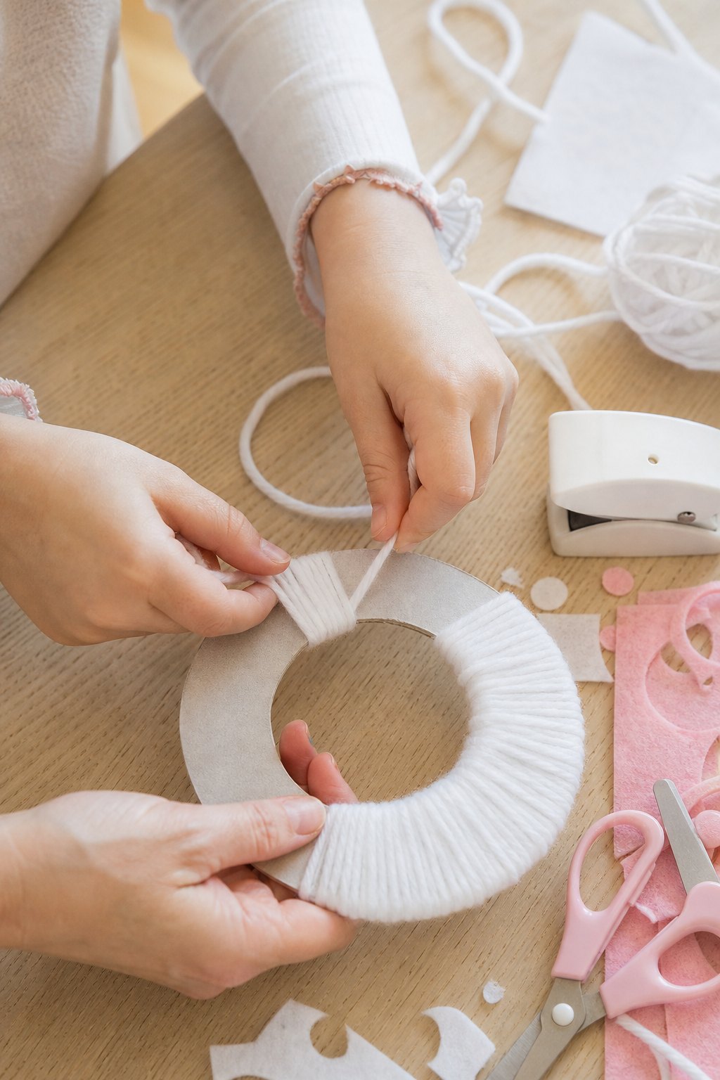 Kinderhände wickeln weiße Wolle um zwei Pappringe für einen Pompon