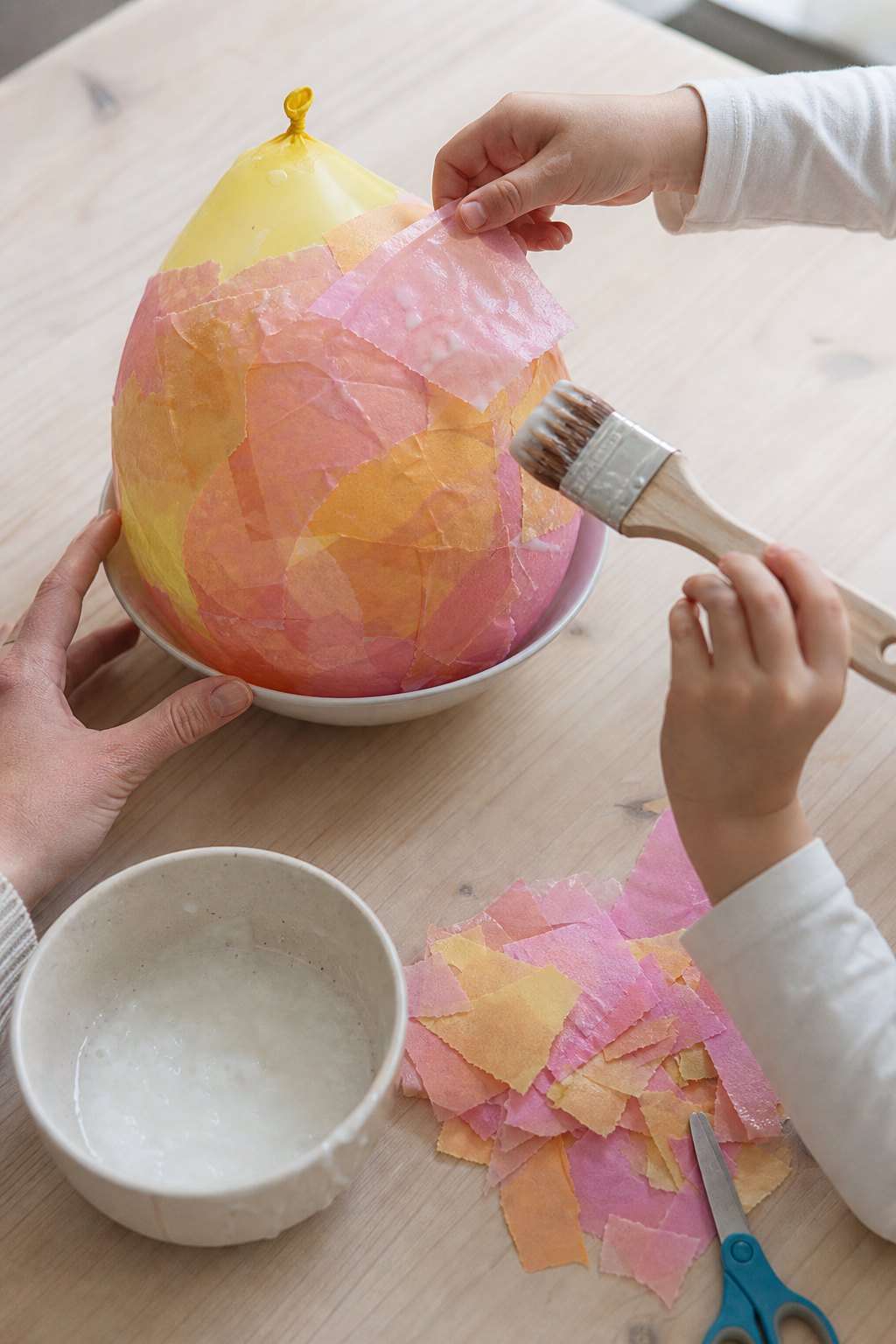 Kinderhände legen Transparentpapier auf den gekleisterten Luftballon