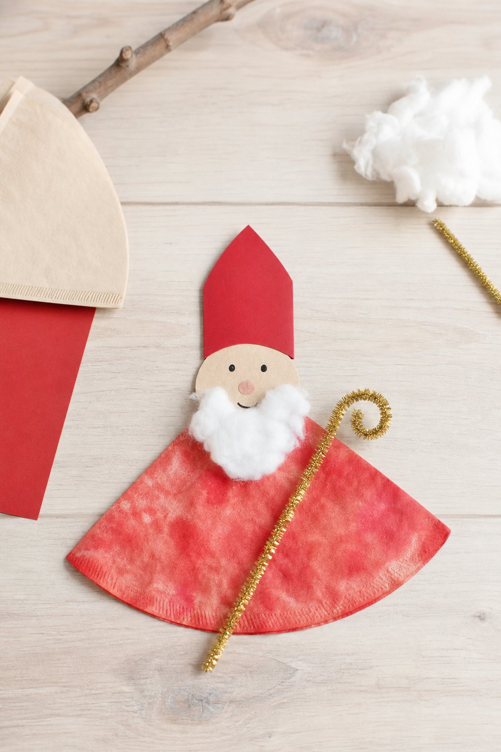Der Nikolaus aus dem Kaffeefilter — Eine flache Nikolausfigur liegt auf einem hellen Holztisch: Der Mantel ist eine Kaffeefil