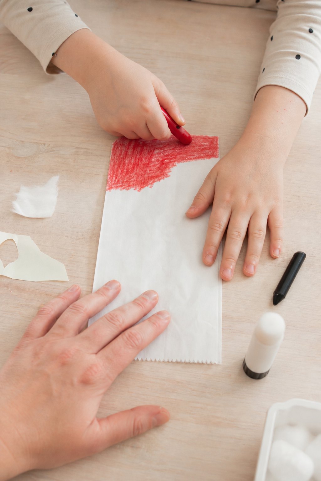 Eine Kinderhand malt den oberen Teil einer Butterbrottüte rot aus