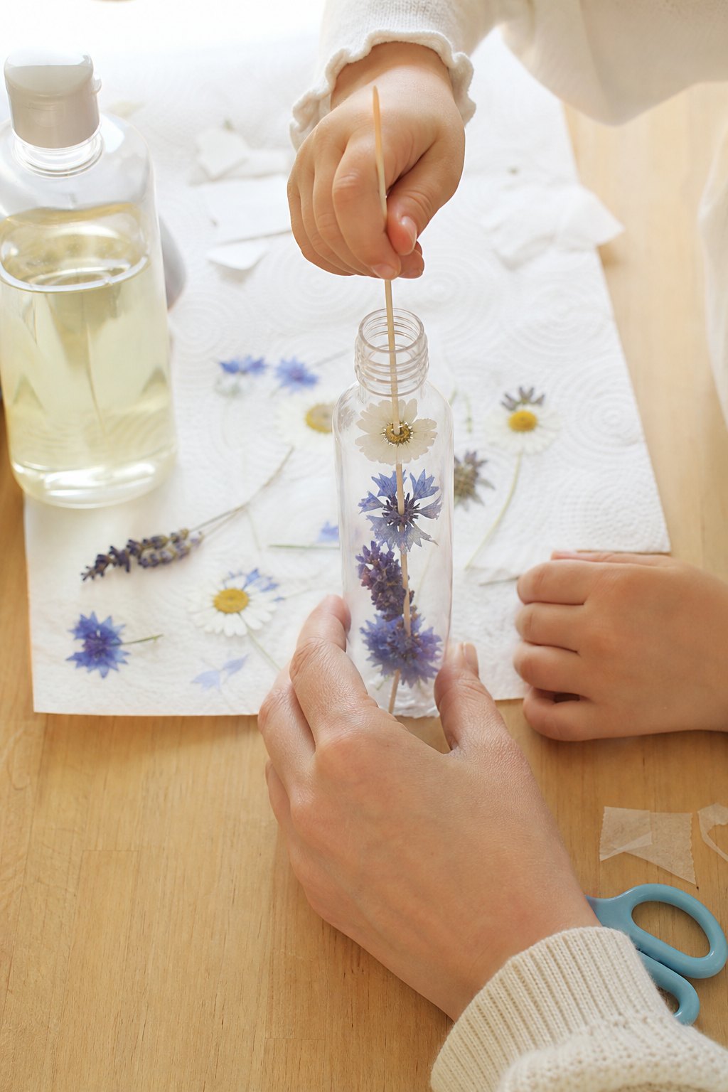 Kinderhand schiebt mit einem Holzspieß eine gepresste Blüte in die Flasche