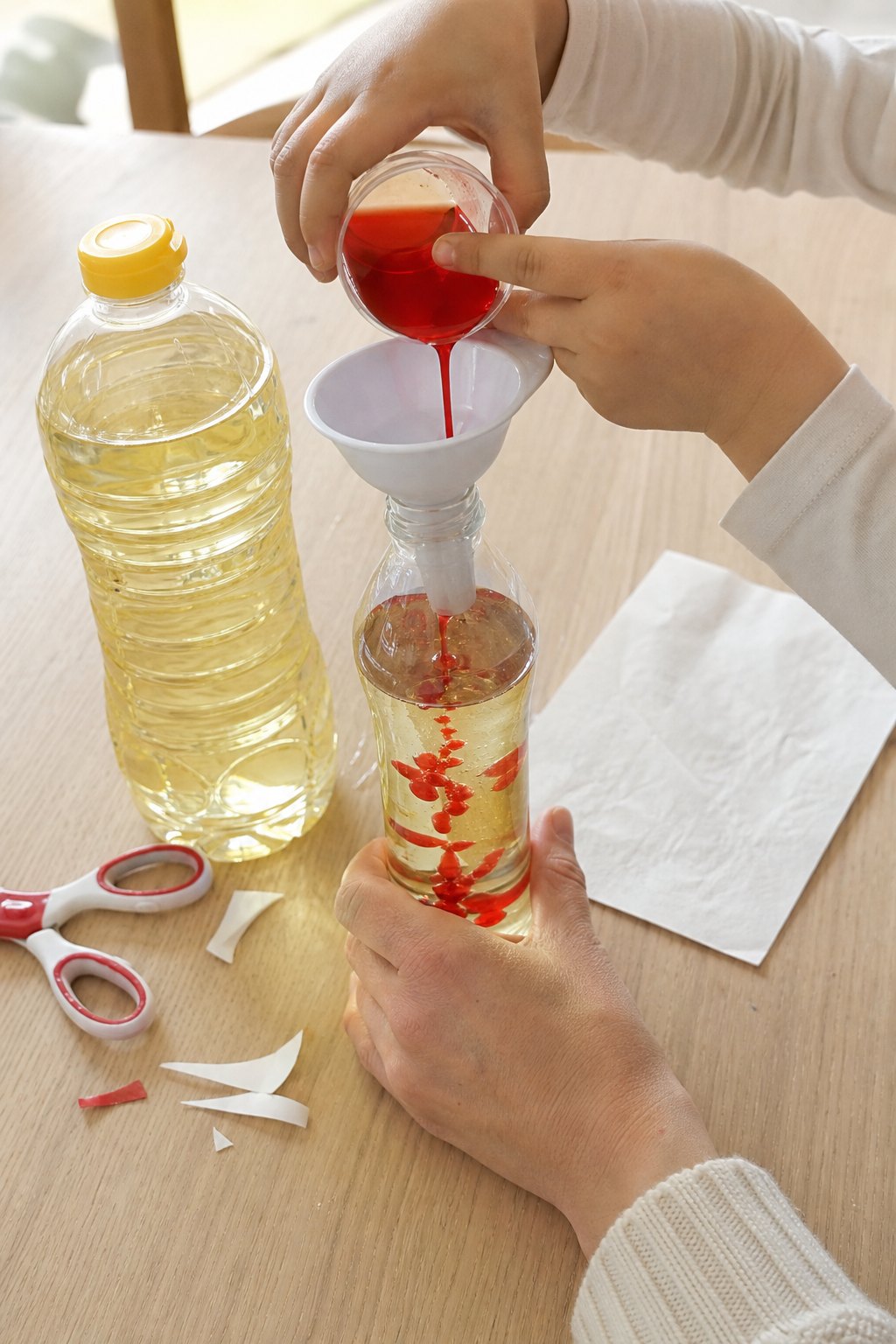 Kinderhände gießen rotes Wasser in eine Flasche mit gelbem Öl