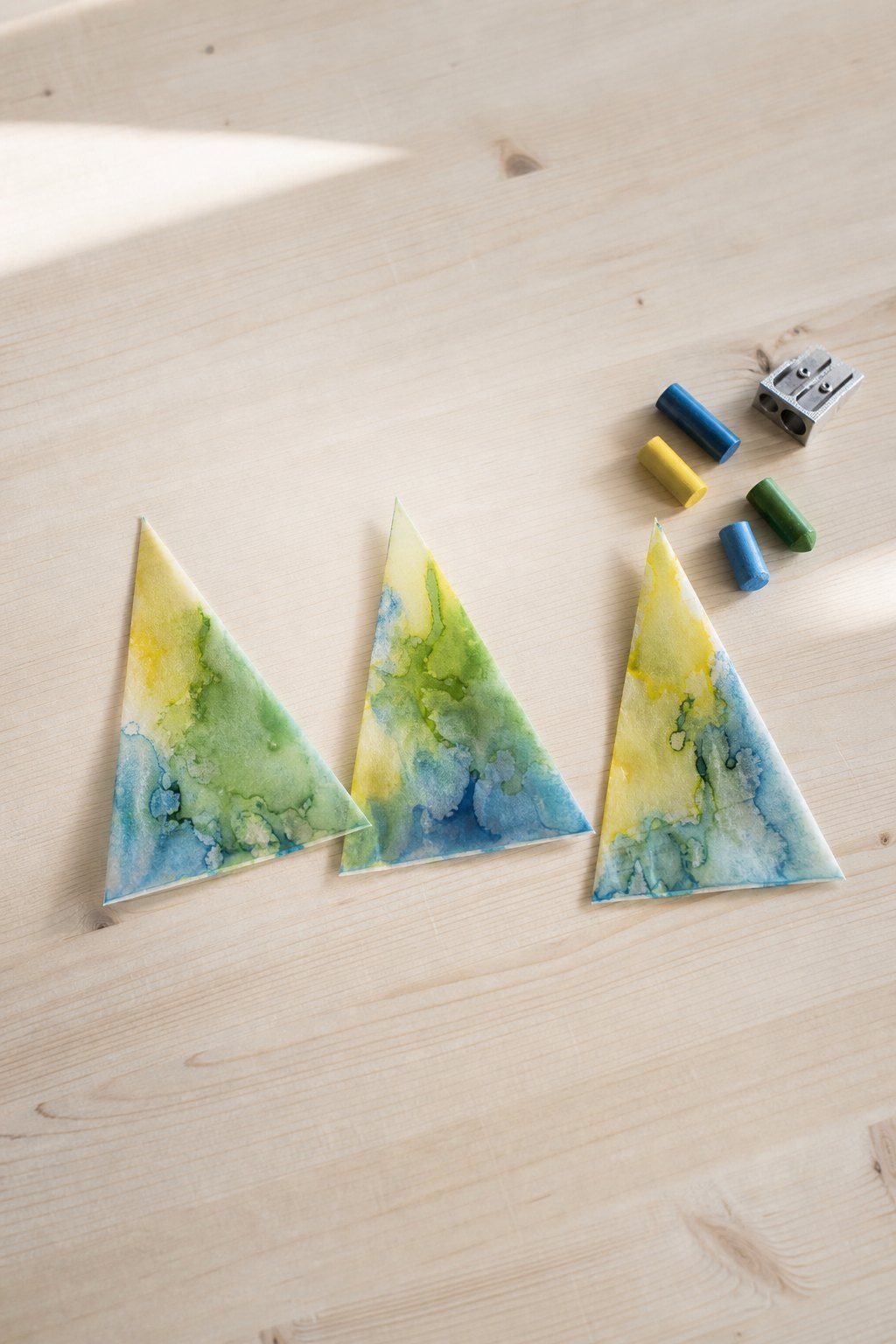 Wachs-Tannen aus Malstiftresten — Drei spitze Dreiecke aus Backpapier, je etwa 8 cm breit und 12 cm hoch, liegen als Tannen a