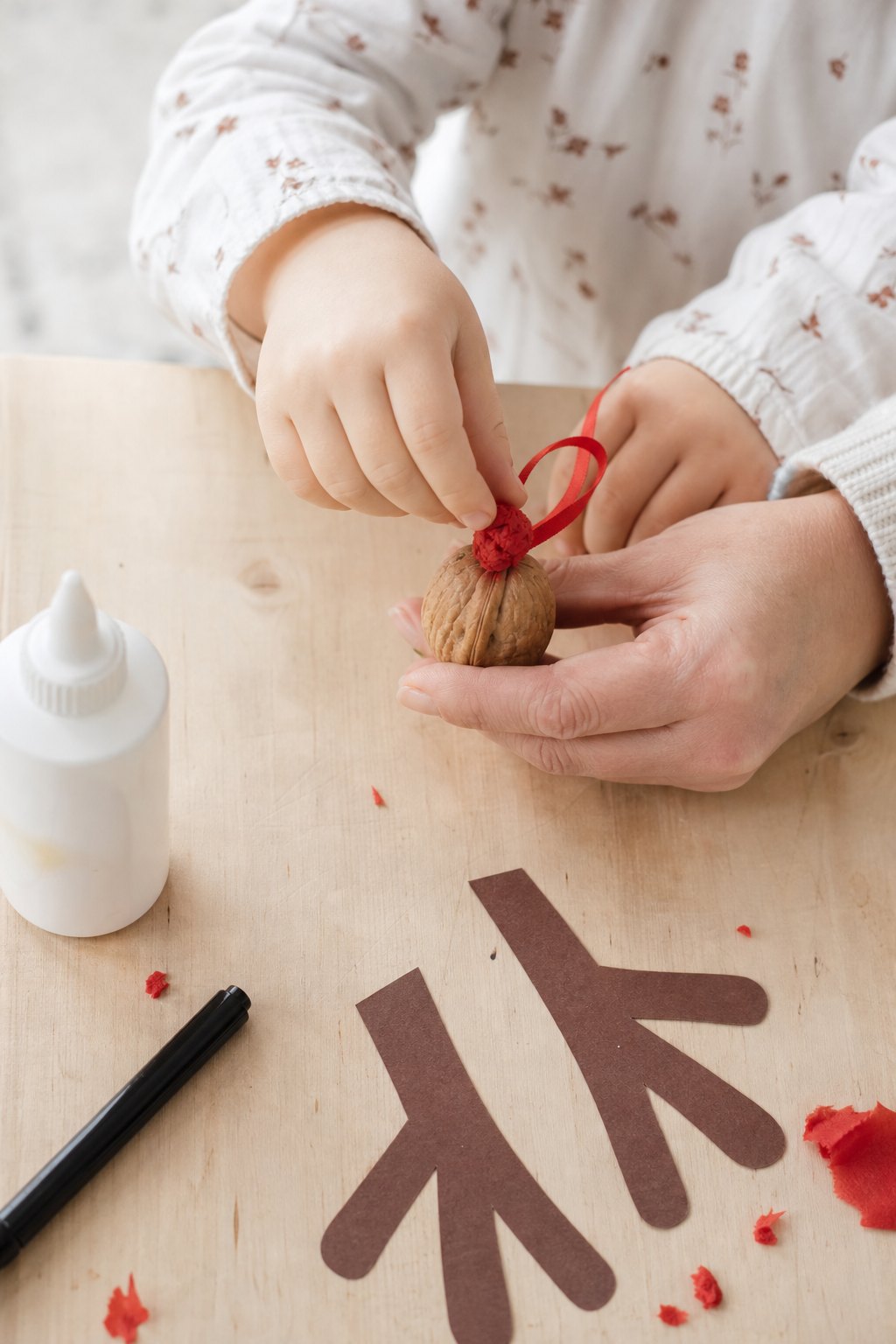 Kinderhand drückt eine rote Papiernase auf die Walnuss, ein Erwachsener hält