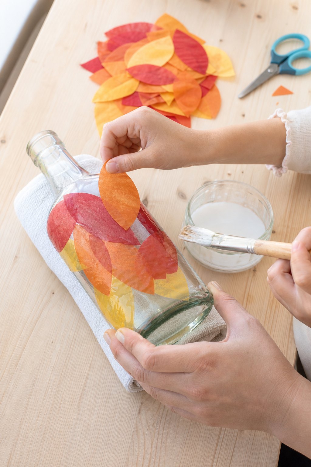 Kinderhand klebt Blätter aus Transparentpapier auf eine liegende Flasche