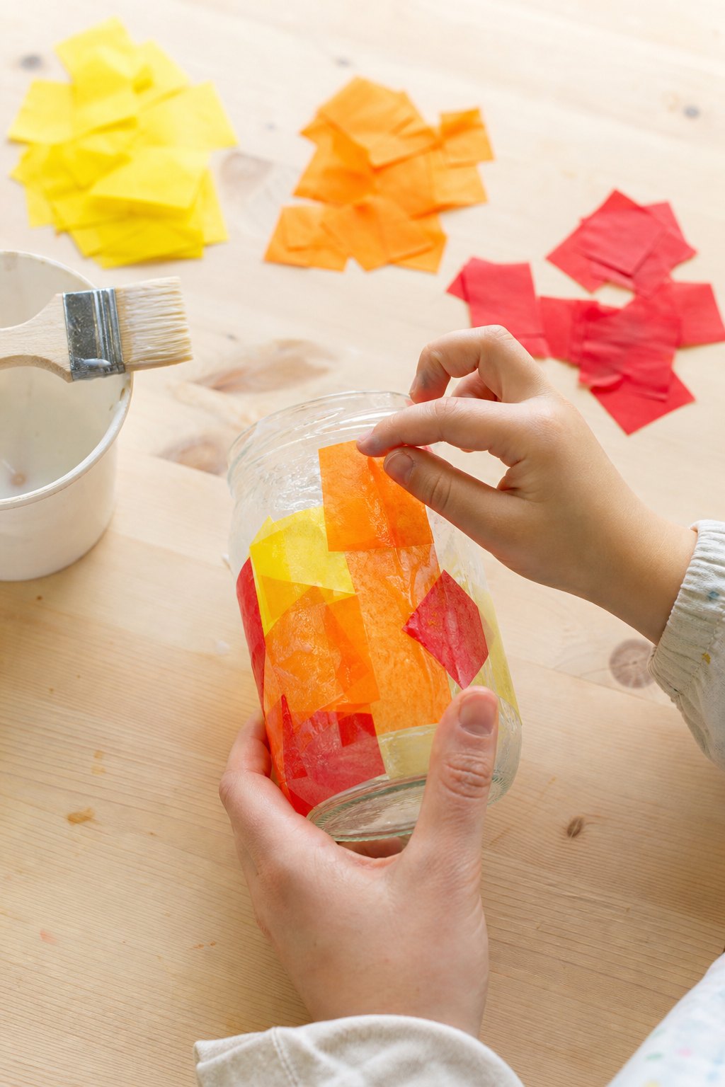 Kinderhand klebt orangefarbenes Transparentpapier auf ein Glas