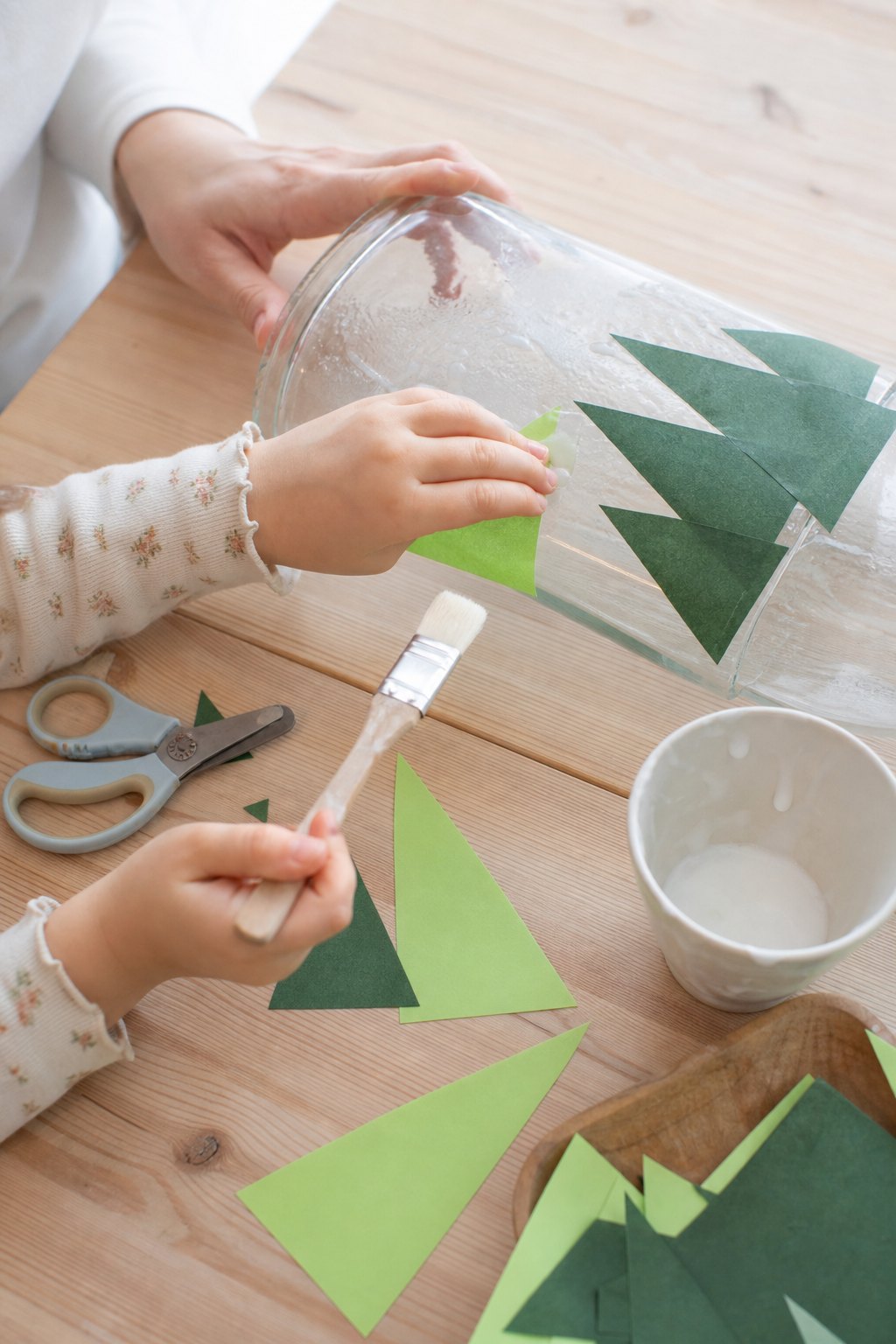 Kinderhand klebt ein grünes Papierdreieck als Tanne auf ein Glas