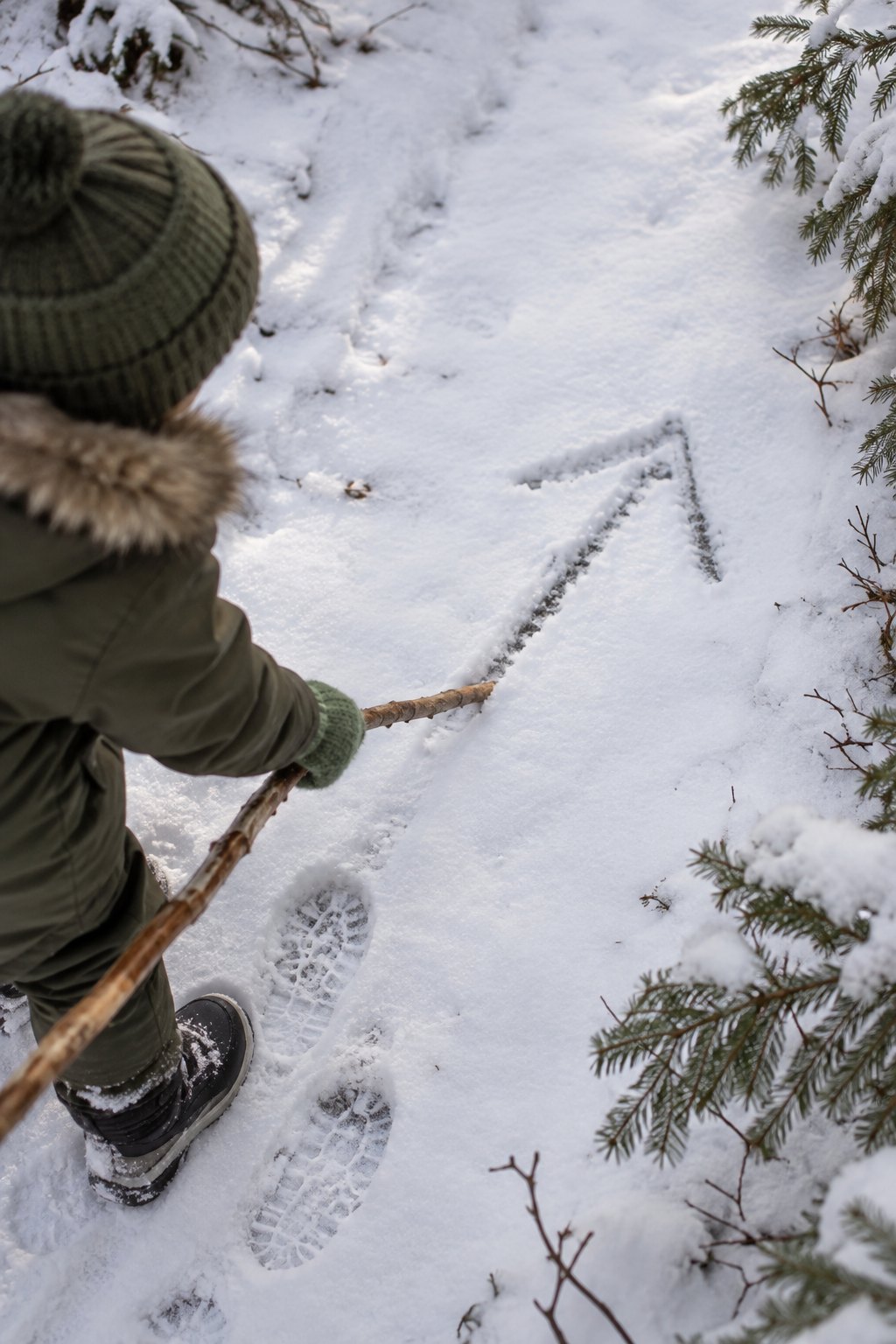 Kinderhand ritzt mit einem Stock einen Pfeil in den Schnee